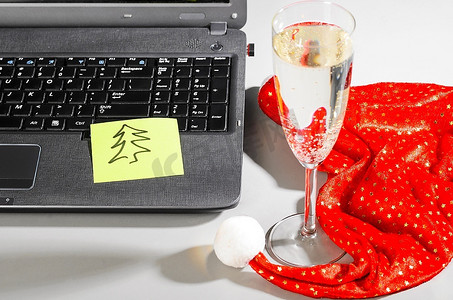 笔记本电脑上有圣诞帽、起泡葡萄酒和云杉，灰色的便条上有云杉
