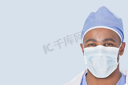 男医生帽子摄影照片_一名男医生在浅蓝色背景下戴口罩的特写
