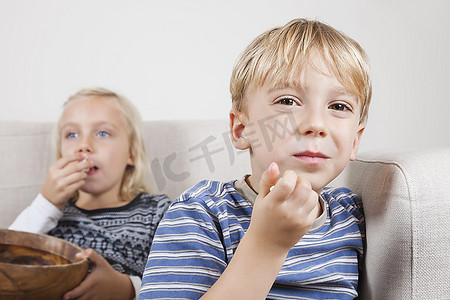 小男孩和妹妹看电视吃爆米花的肖像