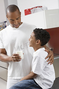 父亲拿着一杯牛奶，在室内拥抱儿子（7-9岁）
