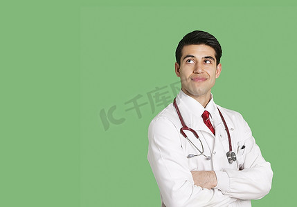 穿着实验室大衣的男医生交叉双臂站着，抬头看着绿色的背景