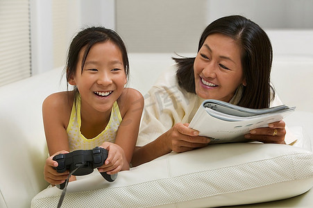 杂志社摄影照片_母女俩在沙发上玩电子游戏、看书