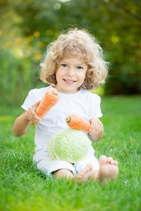 春天公园里，坐在绿草如茵的蔬菜上，开心地笑着的孩子。健康生活方式理念
