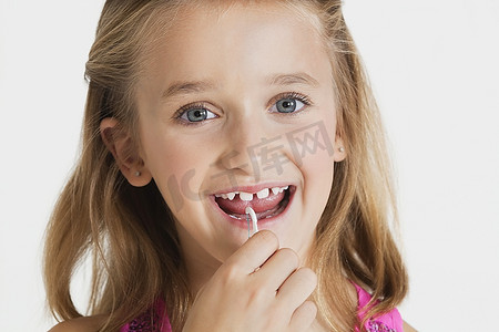 在灰色背景下，年轻女孩用牙线清洁牙齿的肖像