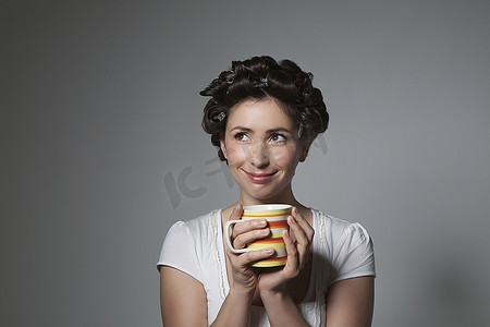 卷发机摄影照片_腼腆的年轻女子拿着卷发机拿着杯子