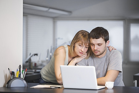 年轻夫妇坐在笔记本电脑在厨房