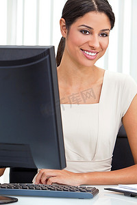 年轻漂亮的拉丁裔拉美裔女性或女商人，穿着时髦的西装，坐在办公室的办公桌前使用电脑