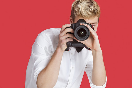 一名年轻男子在红色背景下用数码相机拍照