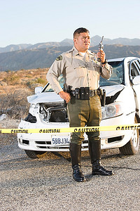 在沙漠中，一名警察在受损汽车前使用无线电