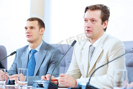 总结发言摄影照片_图像的两个商人坐在桌子上在会议上发言的麦克风