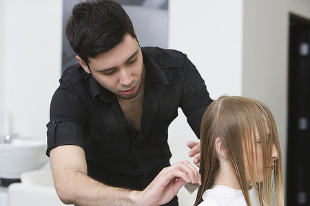 一名男子在理发店为一名年轻女子剪发和梳头