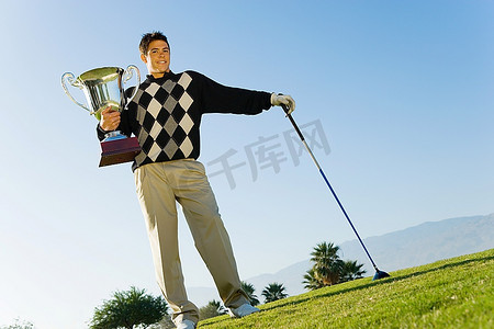 高尔夫球奖杯摄影照片_拿着高尔夫球奖杯的年轻人