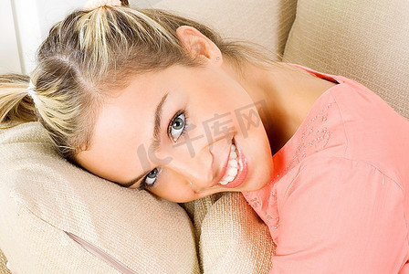 肖像一个漂亮的金发女性穿着晚粉红色礼服坐在沙发上，玩头发