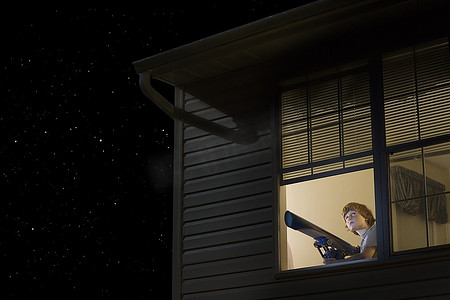 十几岁的男孩开着窗户拿着望远镜看着夜空