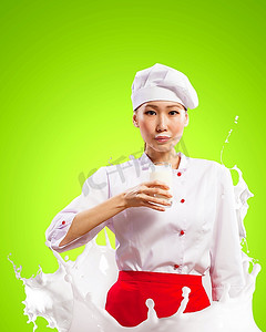 飞溅彩色牛奶牛奶摄影照片_亚洲女厨师手持一杯牛奶，穿着红色围裙，手持牛奶，在彩色背景下飞溅