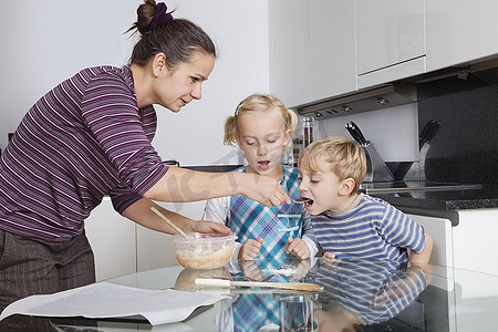 母亲与孩子烘烤和品尝饼干面糊在厨房