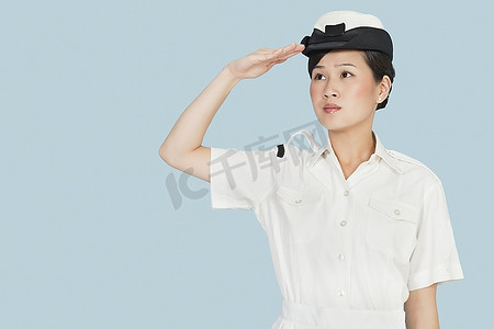 海军敬礼摄影照片_年轻的海军军官看着别处，在浅蓝色的背景下敬礼