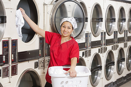 一位快乐的年轻女员工把衣服放进洗衣机的肖像