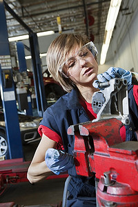 在汽车修理厂的机械部件上，身穿防护工作服的年轻女机械师