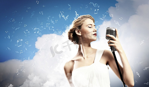 金发女歌手闭着眼睛拿着麦克风在云彩的背景下