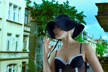 时尚照中的性感美女戴着黑色帽子和内衣站在窗外，背景是古老的宫殿