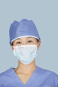 劣质口罩摄影照片_一名女外科医生在浅蓝色背景下戴口罩的特写
