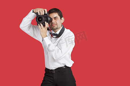 正式红色背景摄影照片_混血男子在红色背景下用数码相机拍照