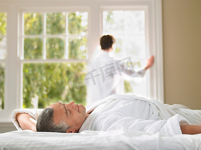 男人躺在床上放松妻子看着背景中的窗户