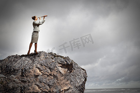 站在岩石顶上用望远镜看的女商人形象