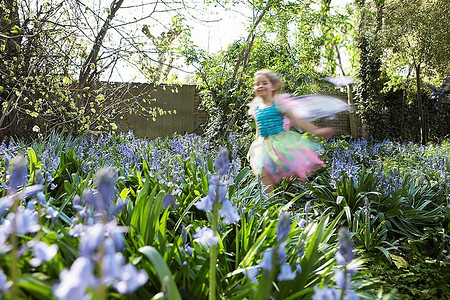 户外运动老外摄影照片_年轻女孩(5-6岁)穿着仙女服装运动模糊在花园里奔跑
