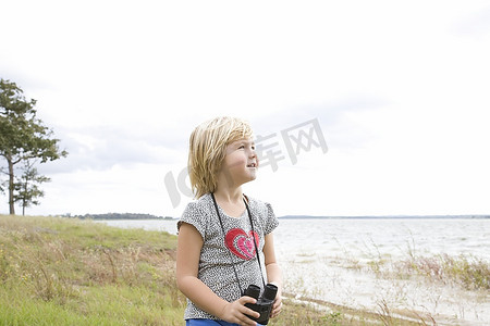 风筒风摄影照片_一个女孩拿着双筒望远镜站在湖边