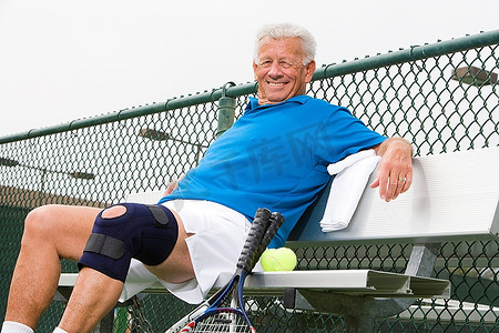 长摄影照片_男子穿着膝盖带在网球场上
