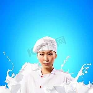 穿着红色围裙的亚洲女厨师站在防止牛奶飞溅的背景下：