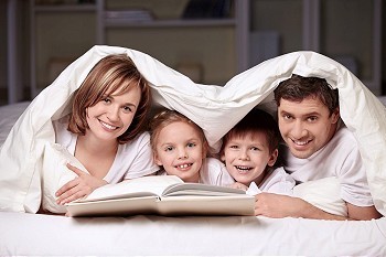 父母带着孩子盖在毯子下，手里拿着一本书