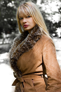 阳光明媚的冬日，美丽的金发女孩在公园里穿着冬夹克和皮毛