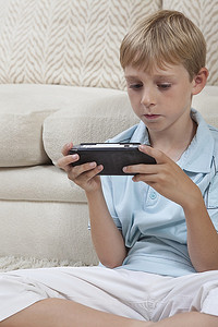 男孩盘腿坐着，拿着便携式游戏机