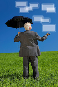 框图形摄影照片_一位商人站在绿色的田野上，撑着伞，看着图形屏幕框的网络概念图