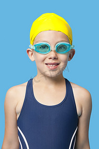 紧身衣摄影照片_蓝色背景上戴着泳镜的快乐年轻女孩的肖像