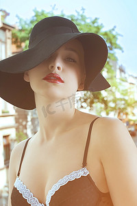一个时尚射击的性感美丽的妇女佩带一顶黑帽子和胸罩在窗口外面与老都市背景在夏天天