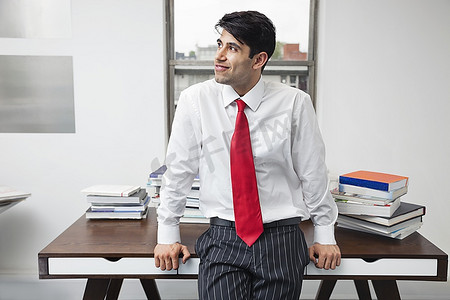 一名印度商人在办公室里靠在办公桌上，目光转向别处
