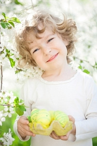快乐的孩子拿着复活节彩蛋映衬着春天的花朵