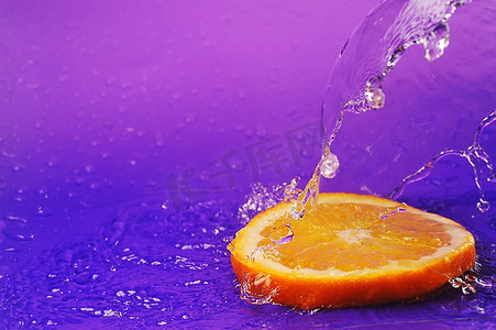 果汁紫色摄影照片_明亮多汁的橙色，在紫色的背景上飞溅