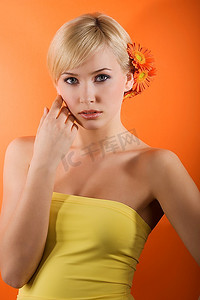 年轻漂亮的金发女孩，黄色上衣，橙色背景下留着非洲菊的发型
