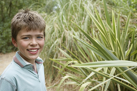 男孩(10-12)站在户外植物旁微笑的肖像