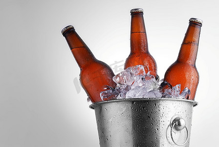 冰桶饮料摄影照片_三个带冷凝的冰桶中的棕色啤酒瓶