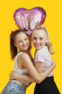 黄色背景上抱着生日气球的两个幸福的年轻女子的肖像