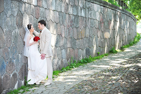 穿着白色礼服的新娘和新郎在老墙附近