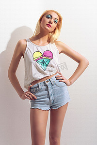 夏天年轻漂亮的金发女郎穿着背心，性感的牛仔短裤在白墙附近摆姿势