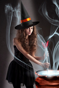 漂亮的大锅摄影照片_万圣节前夕，一位年轻美丽的女巫戴着一顶巨大的黑橙相间的帽子，在一个大锅里制造毒药