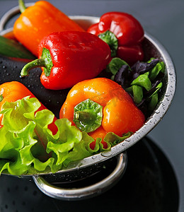 新鲜洗净的新鲜蔬菜在隔绝在黑色背景上的金属滤器中。